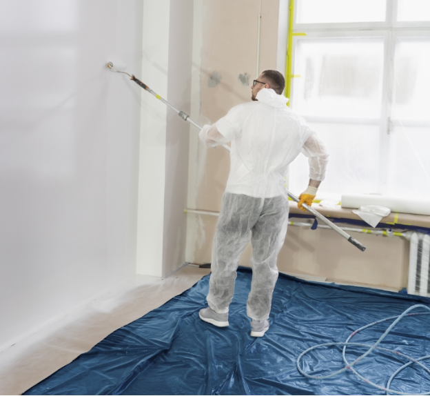 A man is painting the wall with floor covered by drop cloth